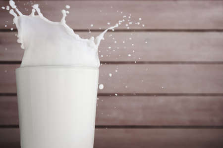 Splash of milk in glass on wood backgroundの写真素材