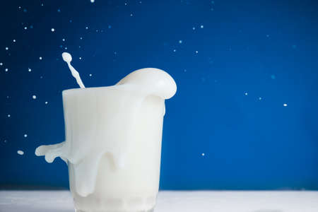 Splash of milk in glass on blue backgroundの写真素材