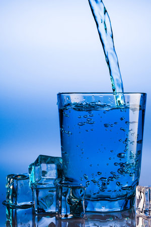 Pouring water into glass with ice cubes