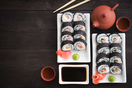 Sushi rolls with salmon and hot tea ceremony on black wooden tableの写真素材