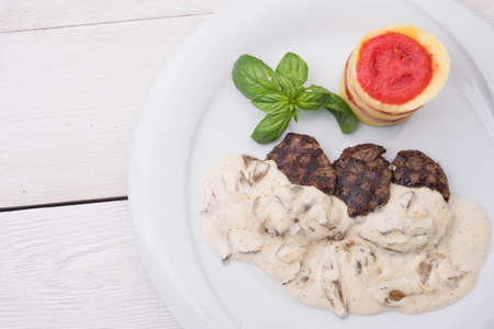 roasted medallions with mushroom sauce, tomato and basil on white wood backgroundの写真素材