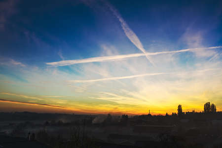 rural sunset with blue and yellow sky and white clouds. fog covered houses.の写真素材