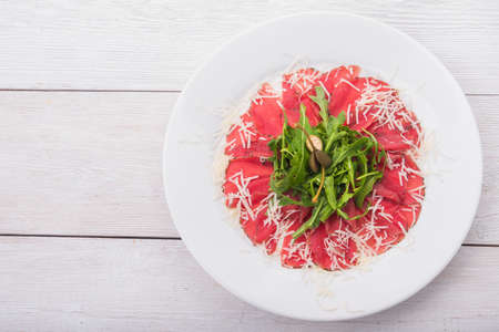 white dish with carpaccio and cheese on white wood backgroundの写真素材