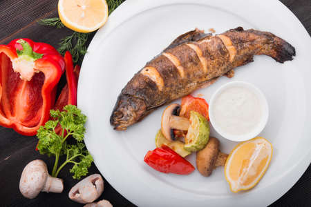 baked fish with lemon and grilled vegetables on white plateの写真素材