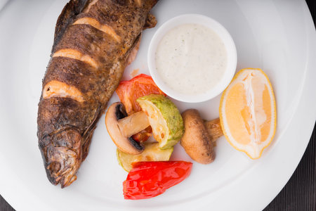 baked fish with lemon and grilled vegetables on white plateの写真素材