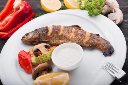 baked fish with lemon and grilled vegetables on white plate