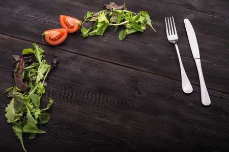 metal knife and fork with green arugula and tomato on dark wood backgroundの写真素材