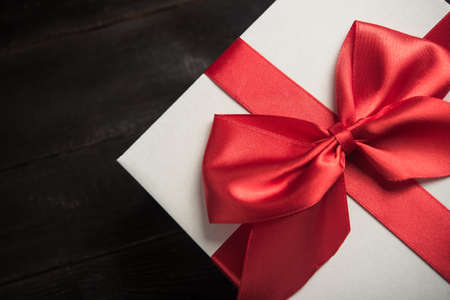 white gift box with red ribbon bow on dark wood backgroundの写真素材