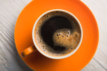 Orange cup of coffee on wooden tableの写真素材
