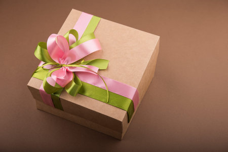 Carton gift box with rose and green ribbon on brown backgroundの写真素材