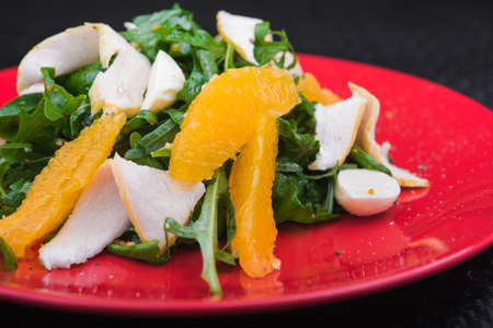 Diet chicken salad with orange and arugula on red plate. restaurant foodの写真素材