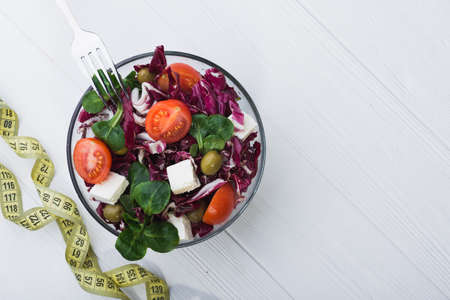 fresh salad in glass bowl with tomato, chees feta and green leaves on wooden table. diet conceptの写真素材