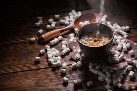 hot coffee poured into a cup with marshmallow dessert on wood tableの写真素材