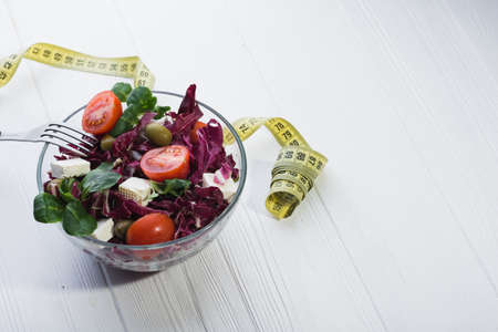 fresh salad in glass bowl with tomato, chees feta and green leaves on wooden table. diet backgroundの写真素材