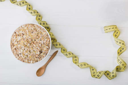 uncooked grain of oatmeal in white bowl with measuring tape. diet concept. healhy foodの写真素材