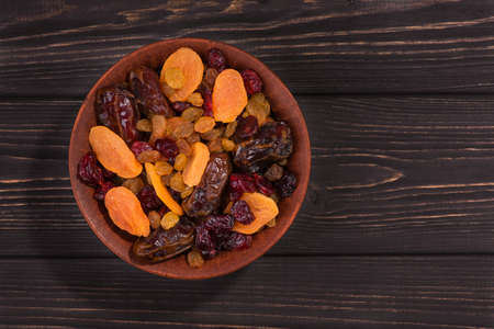 Mix of dried fruit in clay bowl, stand on wooden black tableの写真素材
