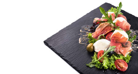 Salad with prosciutto, mozzarella, fresh tomato and arugula on slate plateの写真素材