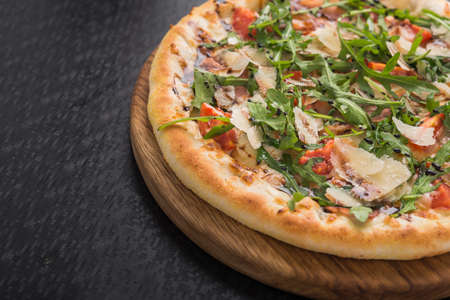 tasty pizza with tomato, cheese, bacon and arugula on wood cut board. black backgroundの写真素材