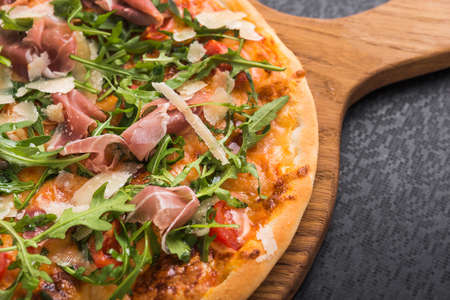 hot italian pizza with prosciutto and arugula on black kitchen tableの写真素材