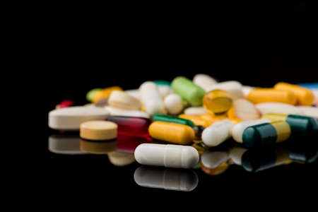 colored pills on black glass background. medical pharmacyの写真素材