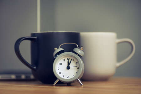 metal old alarm clock with coffee cup on wood table. Break in the office.の写真素材
