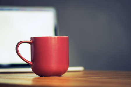 red coffee cup and laptop in office table. business conceptの写真素材
