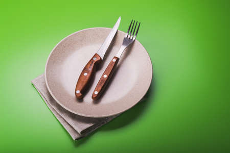 Empty white plate with knife and fork on green background. view from topの写真素材