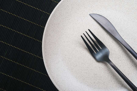 Empty white plate with knife and fork on black table. view from topの写真素材