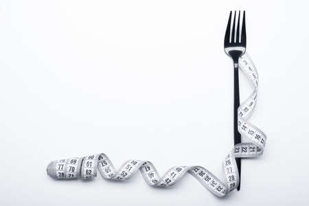 Diet concept, black fork and measuring tape isolated on white backgroundの写真素材