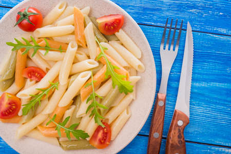 penne pasta with tomato and arugula on white dish. blue background. italian foodの写真素材
