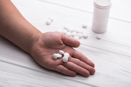 Child hand with white medical pills on wood background. Children treatment