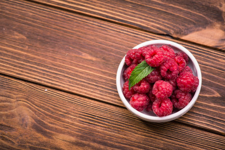 Red fresh raspberry in bowl on wooden table