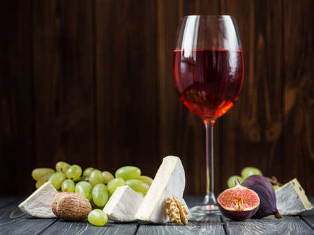 a glass of red wine with snacks of cheese, grapes of figs and nuts on wooden tableの写真素材