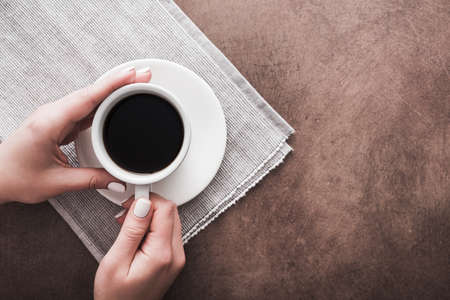 woman holds a white cup of coffee on brown stone tableの写真素材