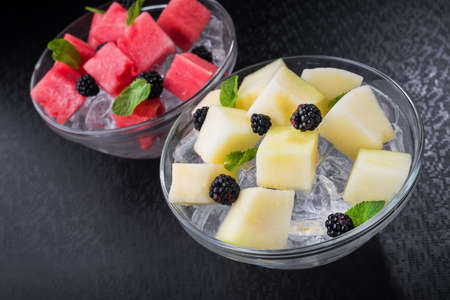 cut melon piece with mint and ice in plate on a black backgroundの写真素材