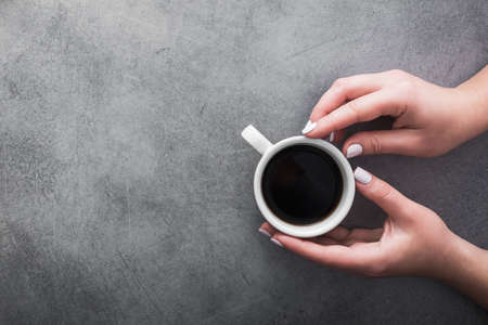 woman in warm sweater holds a white cup of coffee on gray stone table. concept of warming up the drink in coldの写真素材