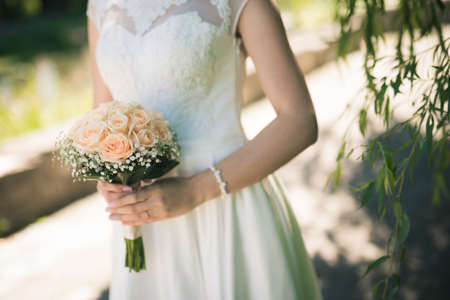 Bride is holding a bouquet of roses in the park at the ceremony, wedding eventの写真素材
