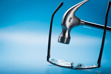 large metal hammer with glasses on blue background. getting rid of glasses and poor eyesightの写真素材