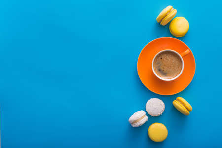 Orange coffee cup with sweet colorful macaroons cake on a blue background, top viewの写真素材