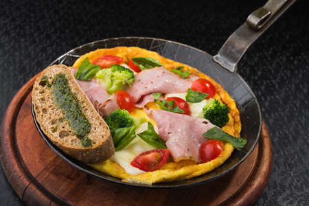 delicious omelet with broccoli, bacon and tomato in metal pan on dark background. italian breakfast foodの写真素材