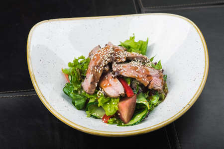 Salad with veal and sesame seeds in a white plate, black backgroundの写真素材