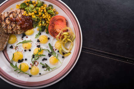 breakfast of quail eggs with tomatoes, chicken fillet corn and broccoli in a plate ob black tableの写真素材