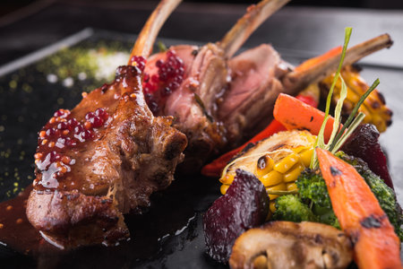 roasted rack of lamb with spice and vegetables on black stoneの写真素材