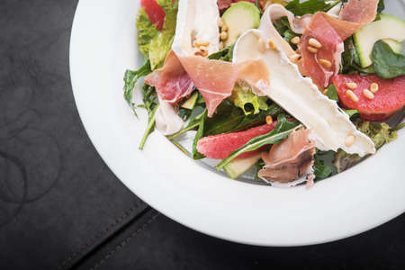 fresh salad with prosciutto and brie cheese, grapefruit and cashew nuts in a white plateの写真素材