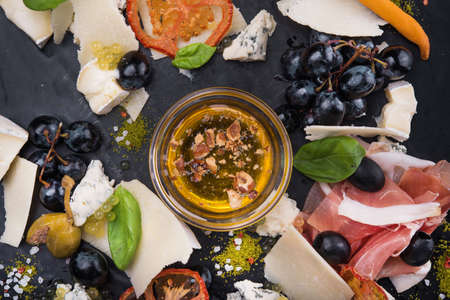 tasty cheese plate with sauce, prosciutto and grapes on black slate board. restaurant foodの写真素材