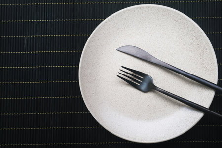 Empty white plate with knife and fork on black table. view from topの写真素材