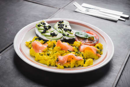 Scramble with avocado, tomatoes and pieces of salmon on a white plate. delicious and hearty breakfast at the restaurantの写真素材
