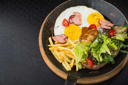 fried eggs with bacon, sausages, tomatoes and salad in a frying pan. juicy and hearty breakfastの写真素材
