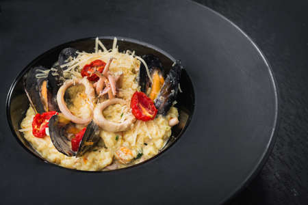 risotto with seafood, mussel and squid and italian cheese in black dish. restaurant serving mealsの写真素材