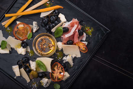 tasty cheese plate with sauce, prosciutto and grapes on black slate board. restaurant foodの写真素材